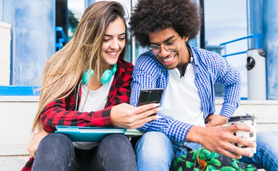 Trilce UCV App Dos estudiantes universitarios sonriendo mientras miran un teléfono celular en el campus de la Universidad César Vallejo