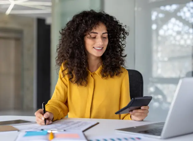 Mujer usando una calculadora y escribiendo en sus documentos impresos