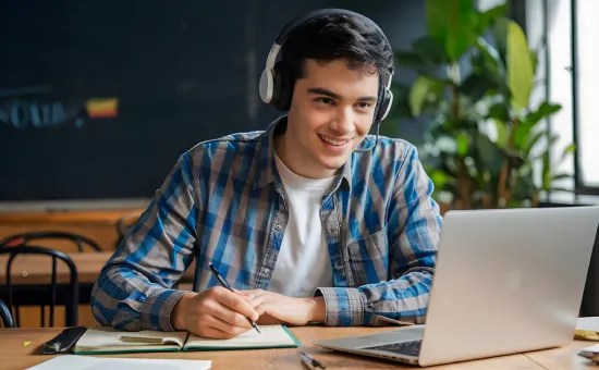 Curso de especialización vs Diplomado Joven con audífonos tomando notas frente a su computadora portátil