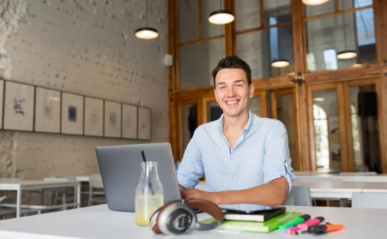 ¿Cómo la universidad puede ayudarte a conseguir empleo más rápido? Estudiante universitario sonriente trabajando en su laptop en un entorno moderno